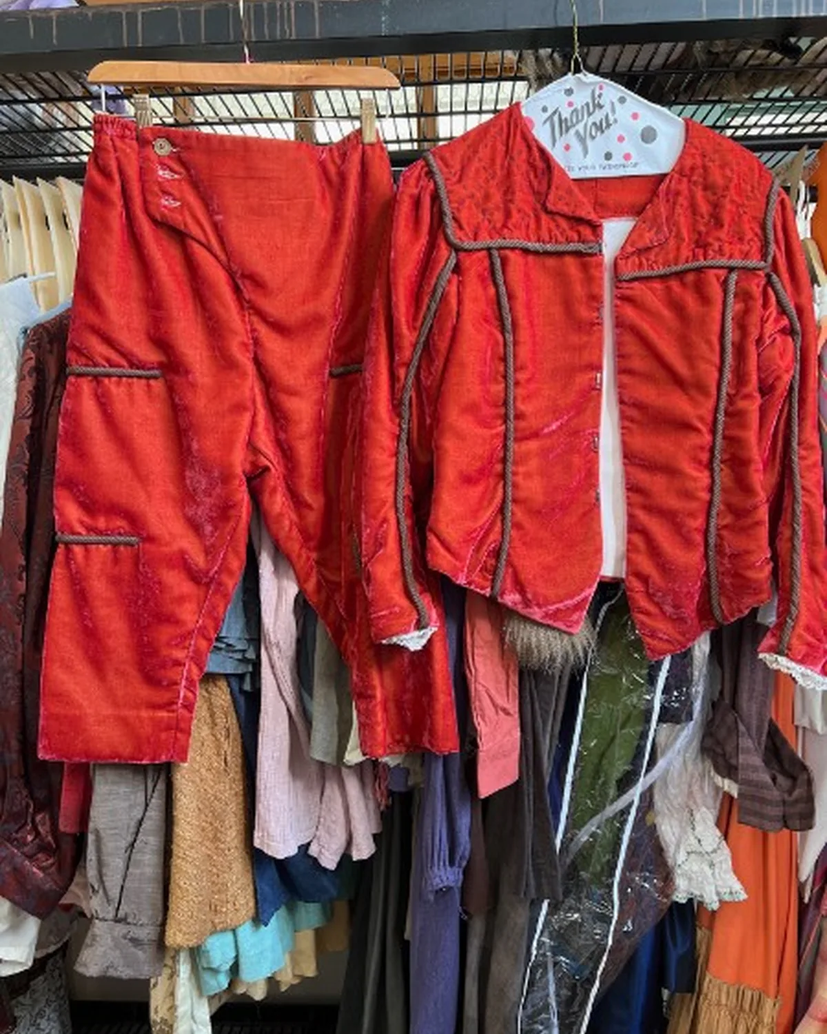 Red velvet stage costumes with corded trim hanging in the shop